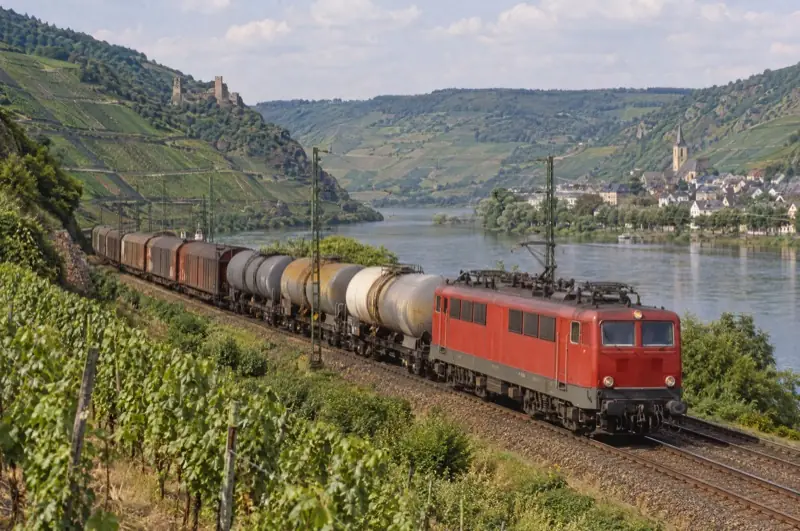 Rote Elektrolok mit Kessel- und gedeckten Wagen in einem Flusstal mit Weinbergen