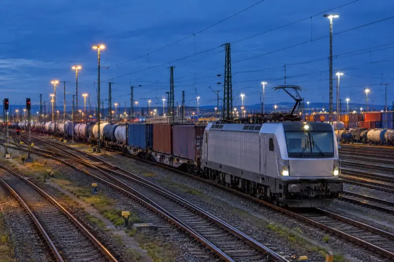Moderner Güterzug mit Kessel- und Containerwagen in einem Rangierbahnhof zur blauen Stunde